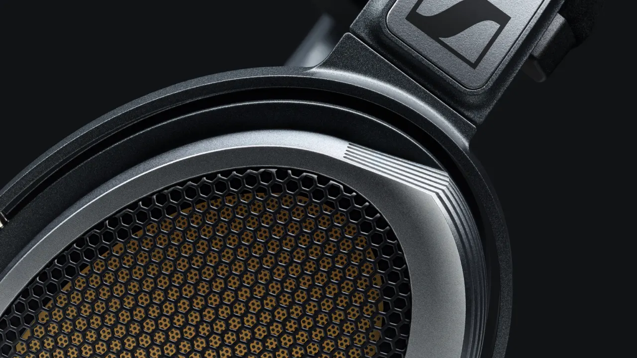 Close-up of a high-end headphone ear cup with a metallic grille and honeycomb pattern, highlighting fine details and the Sennheiser logo on the headband against a dark background.