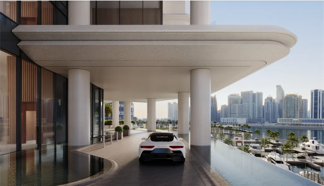 A sleek white sports car is parked under a modern, covered driveway by a waterfront building, with high-rise buildings and a marina filled with yachts visible in the background.