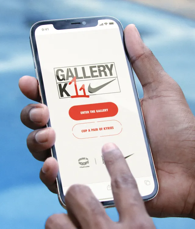 A person holds a smartphone displaying a Nike app screen with “Gallery K11” branding, offering options to enter the gallery or cop a pair of Kyries, by a blurred blue background.