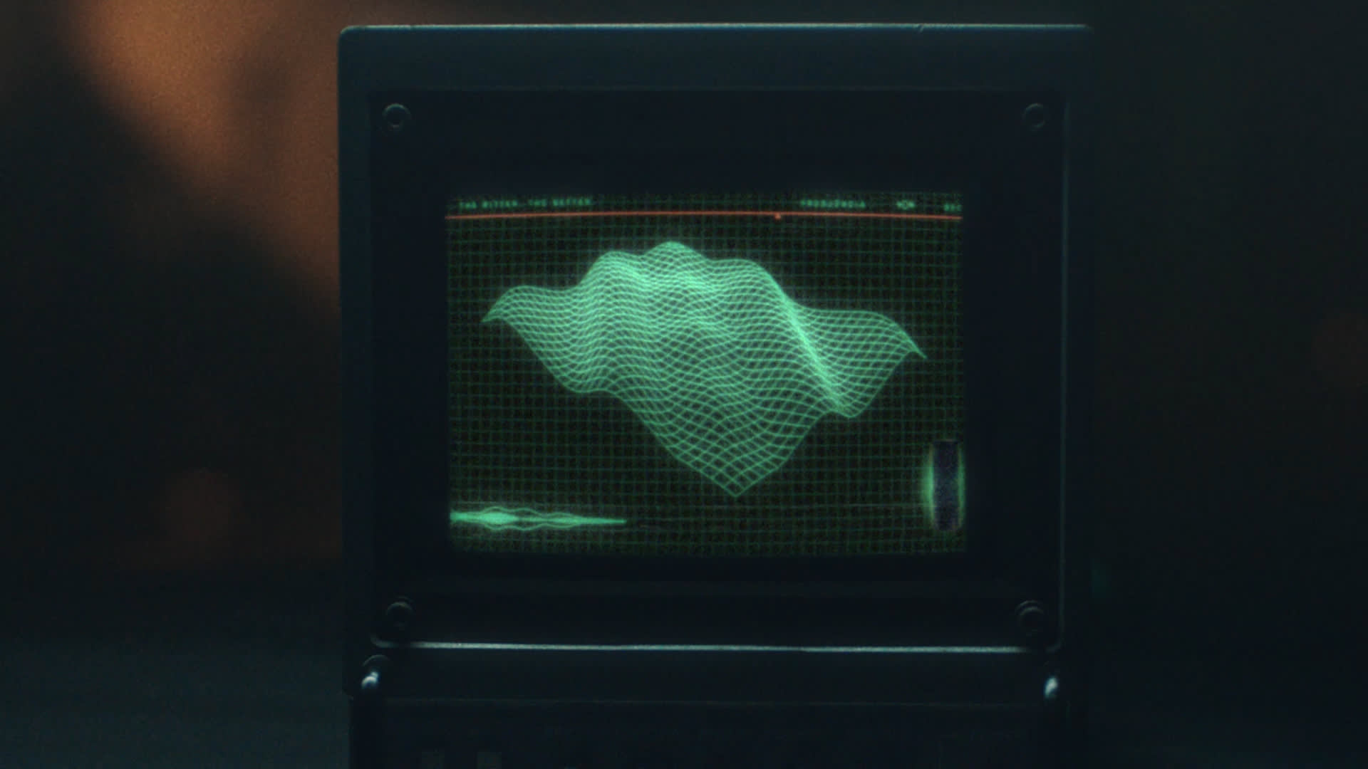A computer monitor displays a green 3D wireframe waveform on a grid background, resembling a digital topographic map or audio visualization. The screen has a retro, sci-fi appearance.