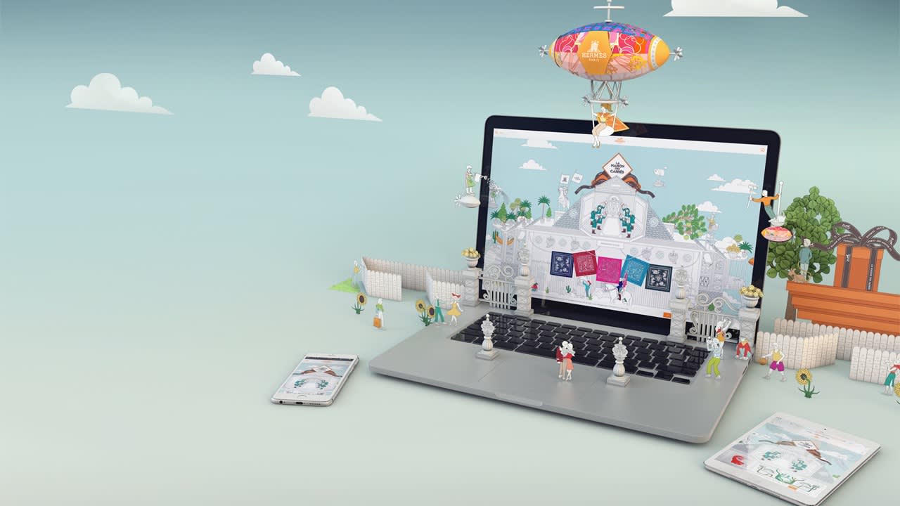 A whimsical scene with miniature people and structures emerging from a laptop screen, with clouds, a blimp, and small trees around. Nearby, a smartphone and tablet display similar designs on their screens.