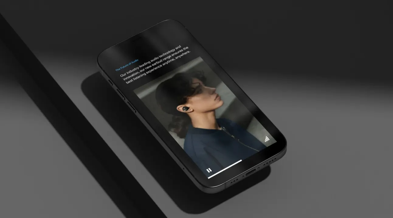 A smartphone lying on a dark surface displays a music or podcast app featuring a photo of a person with short hair wearing wireless earbuds. The screen shows playback controls at the bottom.