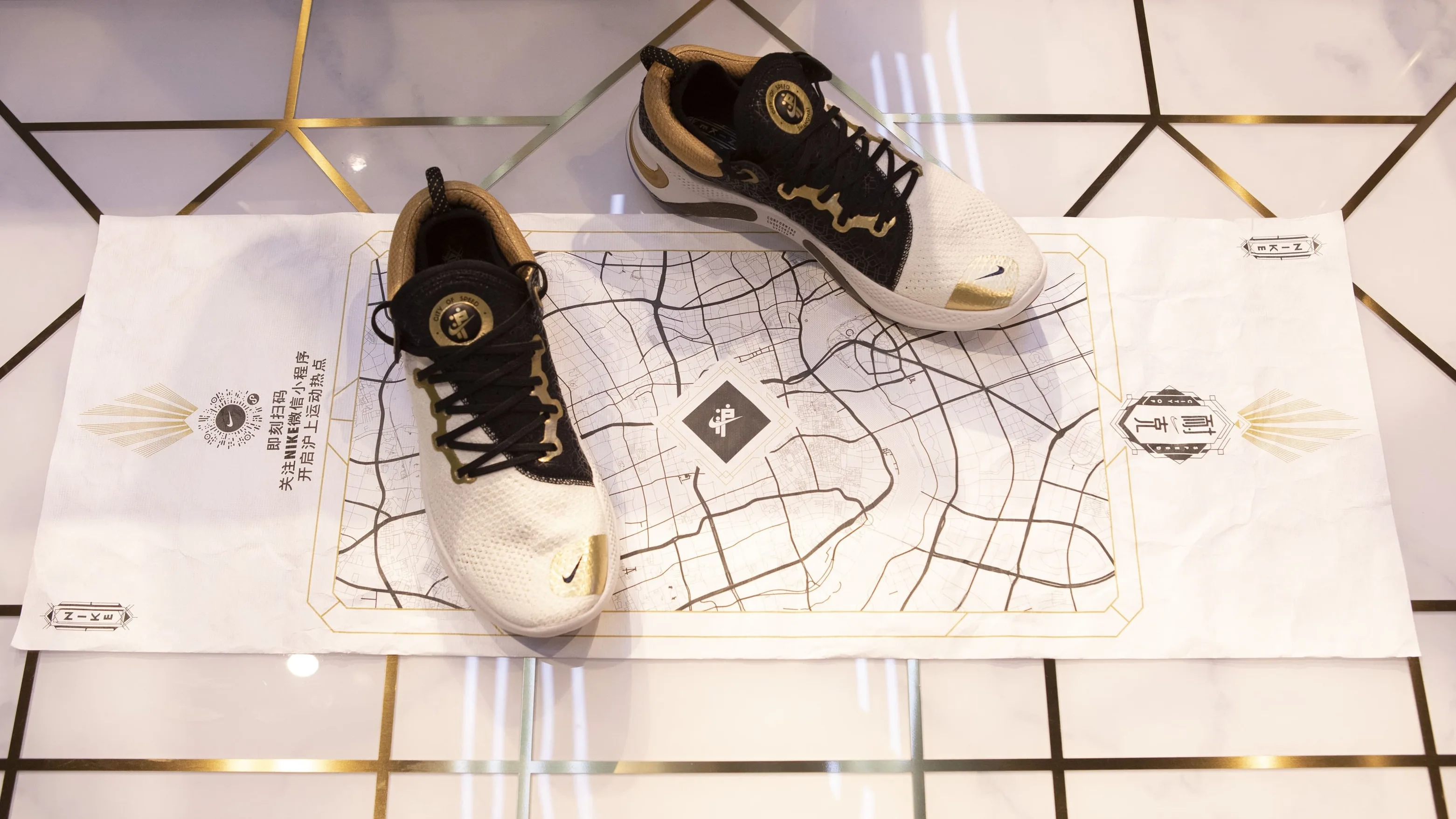 A pair of white and black Nike sneakers displayed on a wrinkled city map spread over a gold-accented tiled floor. The shoes are positioned side by side, partly covering the maps central area.