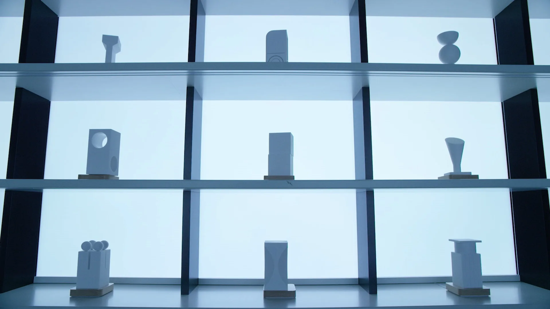 A backlit display shelf showcases nine minimalist abstract white sculptures, each with unique geometric or organic shapes, arranged in a three-by-three grid against a bright, modern background.