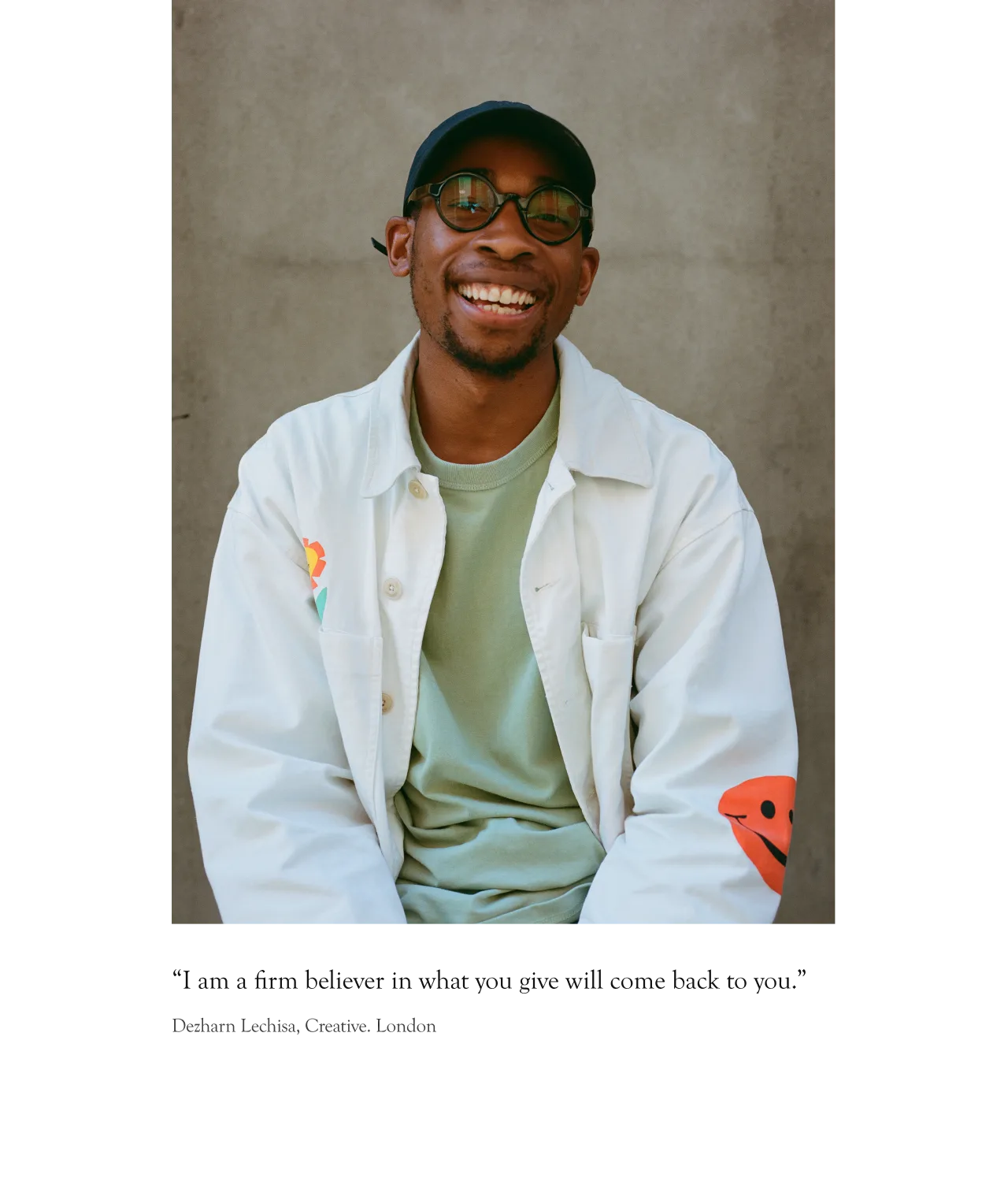 A smiling man wearing glasses, a dark cap, and a light jacket over a green shirt sits against a plain background. Under the image is a quote and the name Deshawn Lechis, Creative, London.