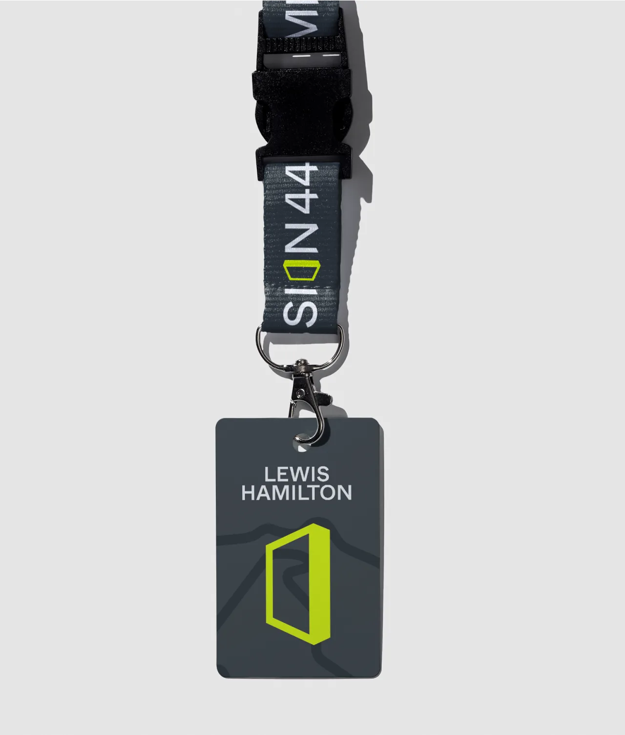 A black lanyard with SON44 in white text holds a dark gray ID badge labeled LEWIS HAMILTON above a yellow geometric logo, all set against a light gray background.