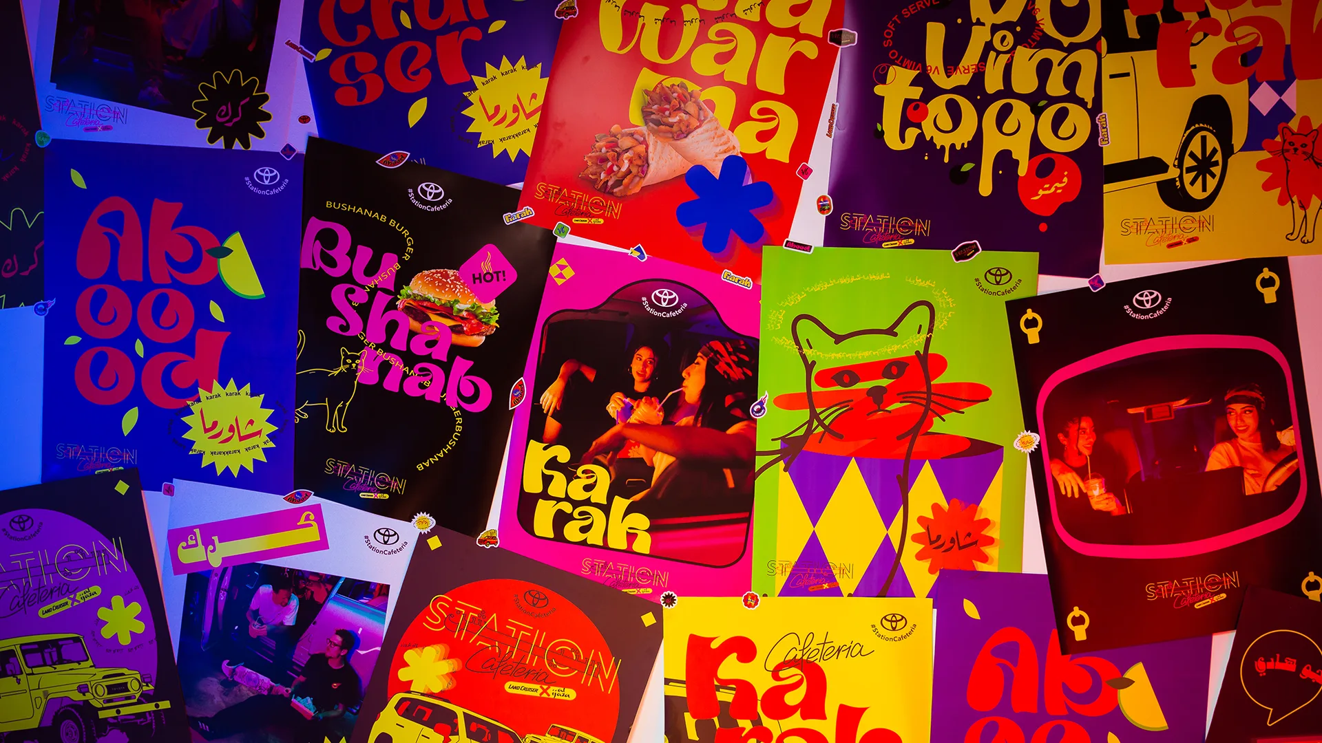 A colorful wall covered with vibrant, neon posters featuring playful typography, stylized food images, cartoon illustrations, Arabic and English text, and people in lively, retro-themed scenes.