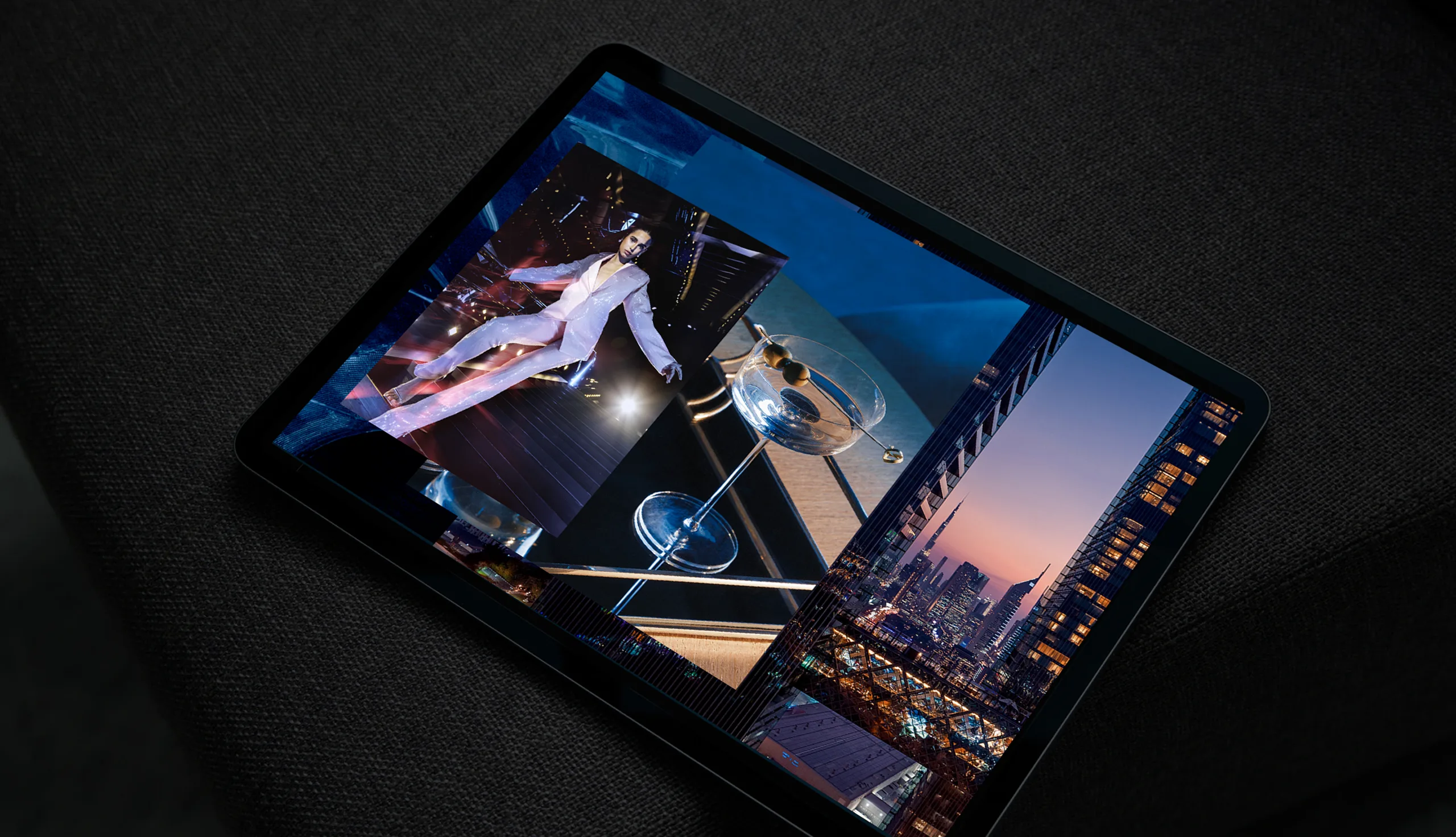 A tablet resting on a dark fabric surface displays a collage of modern architectural images and a person in a white suit posing dramatically next to a large mirrored installation.