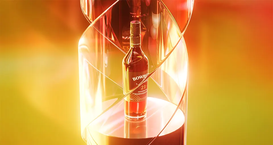 A bottle of Bowmore 21-year-old whisky stands on a round platform, illuminated by golden and orange light, surrounded by a spiral-shaped, transparent ribbon-like structure.
