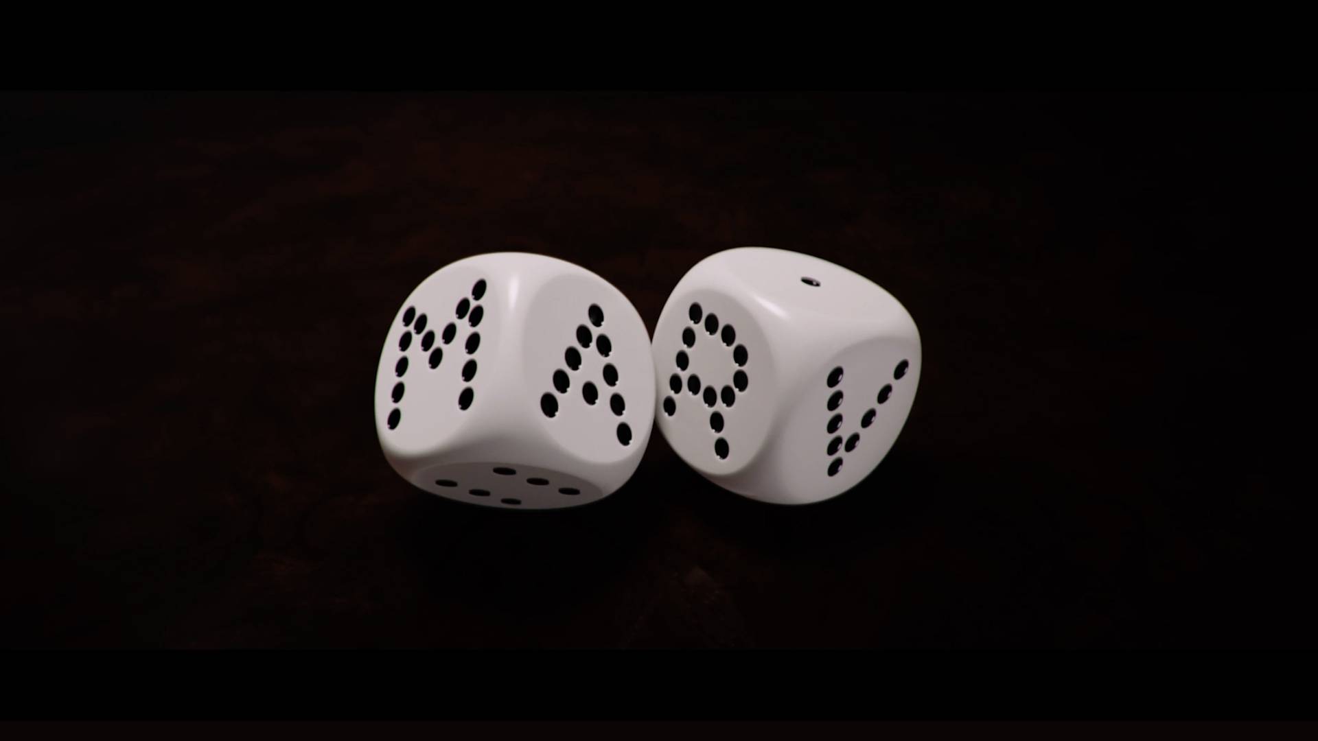 Two white dice display black dots arranged to form the word MAP on a dark brown surface.