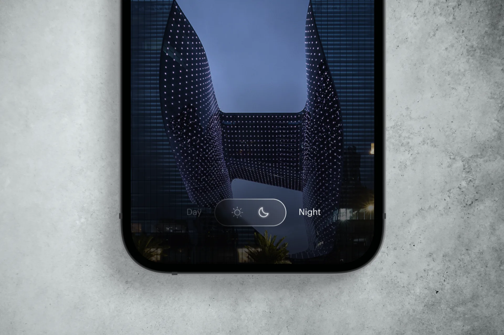 A smartphone screen displays a modern building at night, with the camera mode set to Night. The phone rests on a textured, light gray surface.