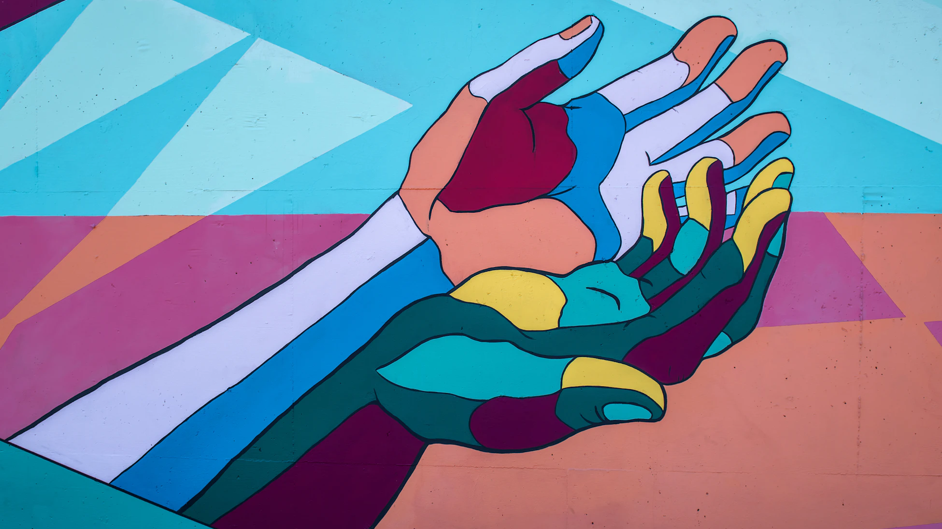 A colorful mural of two open hands overlapping, painted in bold geometric shapes and bright hues of blue, pink, teal, yellow, orange, and red against a pastel background.