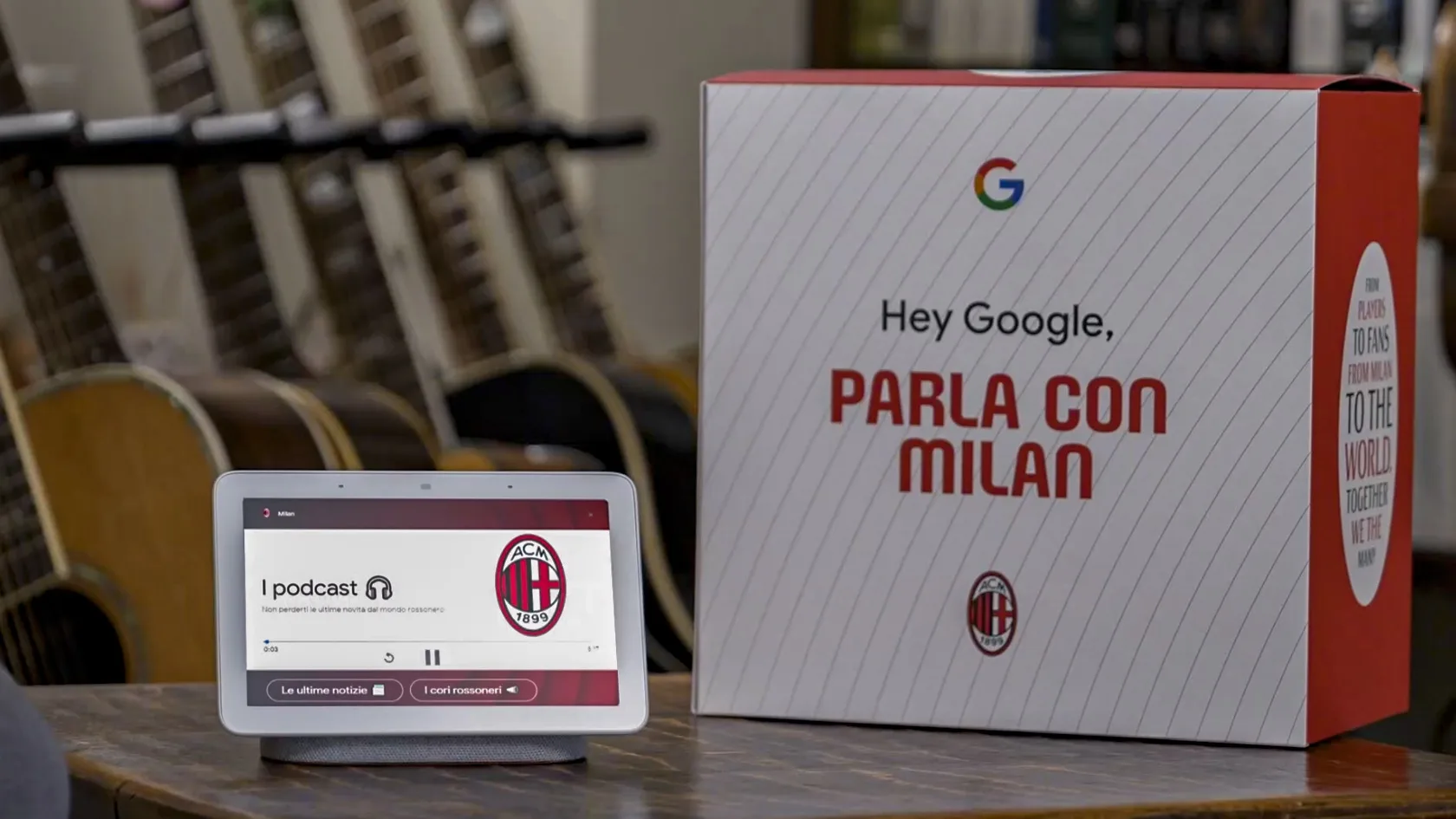 A Google smart display shows an AC Milan podcast, next to a box labeled Hey Google, Parla con Milan with AC Milan and Google logos. Several guitars are blurred in the background.
