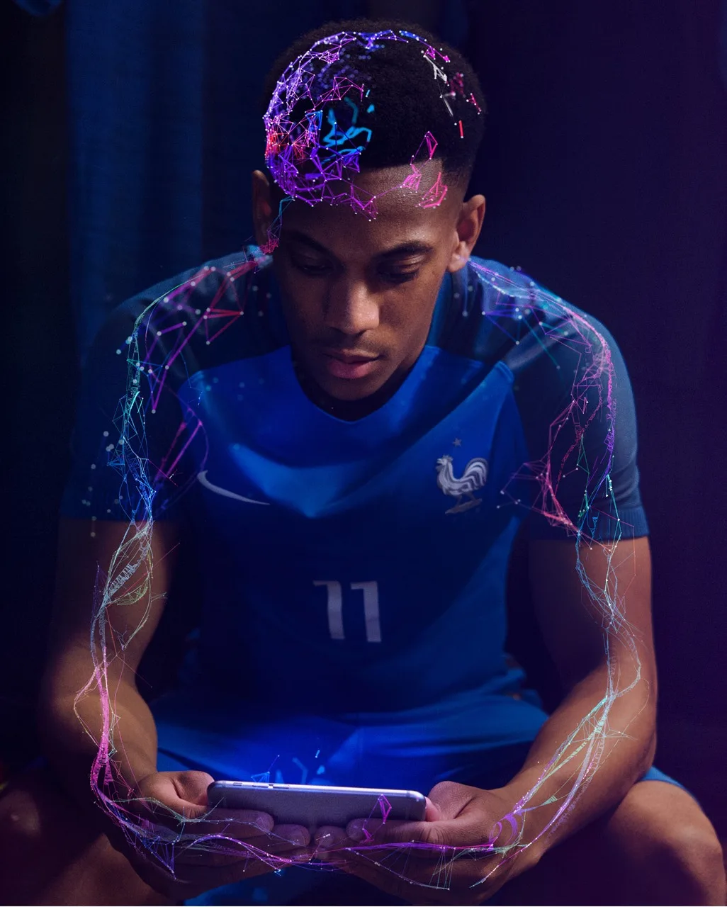 A male soccer player in a blue jersey sits and looks at a tablet, with colorful digital patterns and neural network graphics glowing around his head and arms, symbolizing technology and connection.
