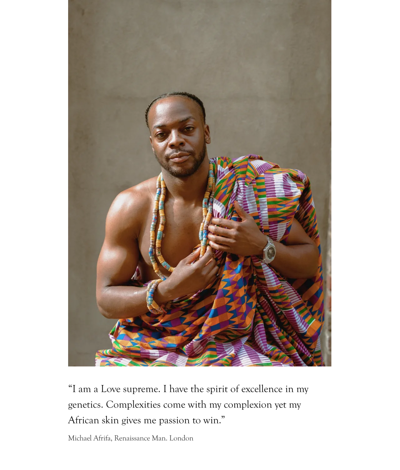 A man wearing a vibrant, multicolored kente cloth and beaded necklace sits confidently, looking at the camera with one hand on his chest and the other resting on his lap against a neutral background.