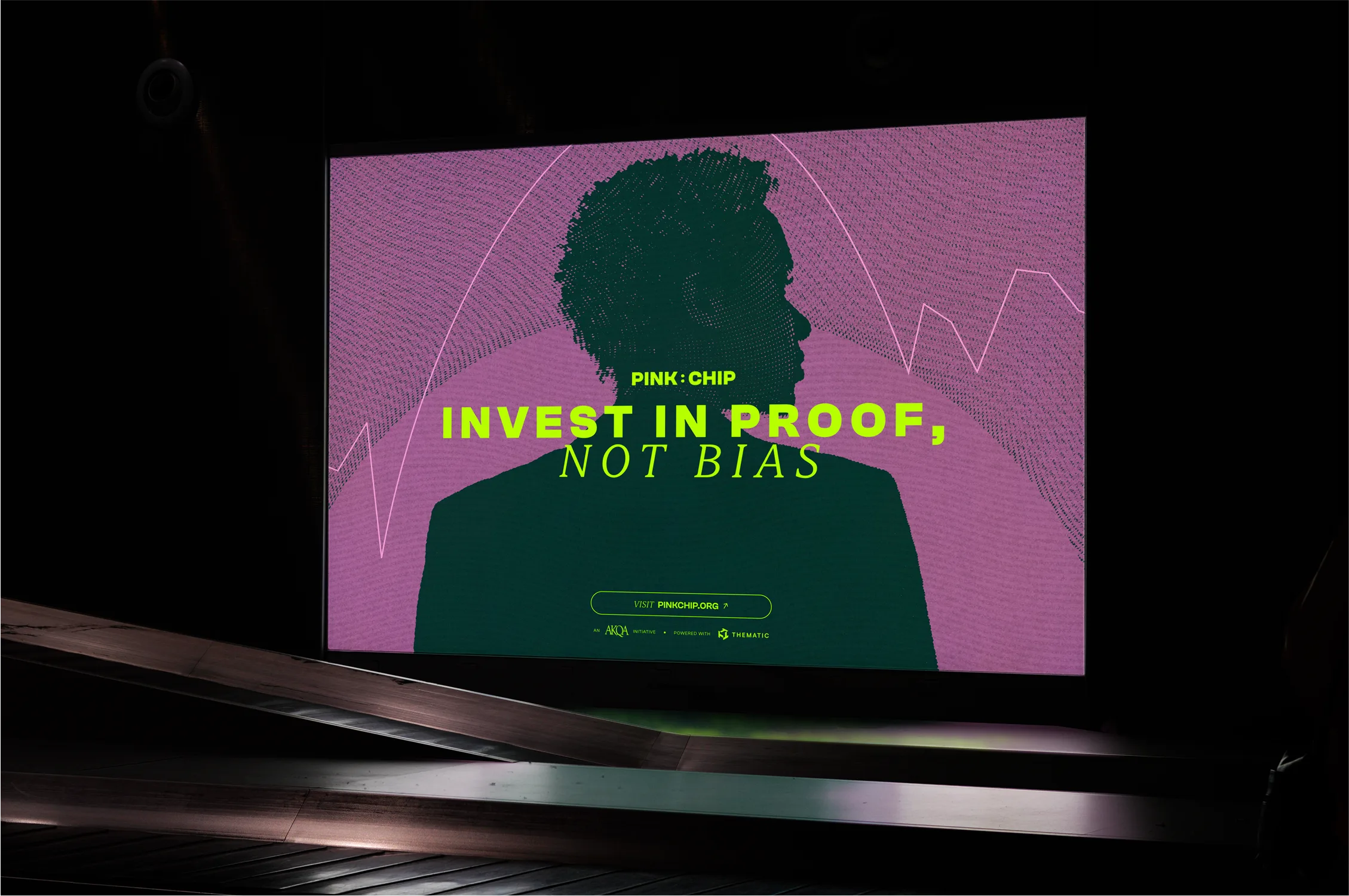 A digital billboard displays the silhouette of a person with text overlay: PINK CHIP. INVEST IN PROOF, NOT BIAS in green and pink, with abstract lines in the background.