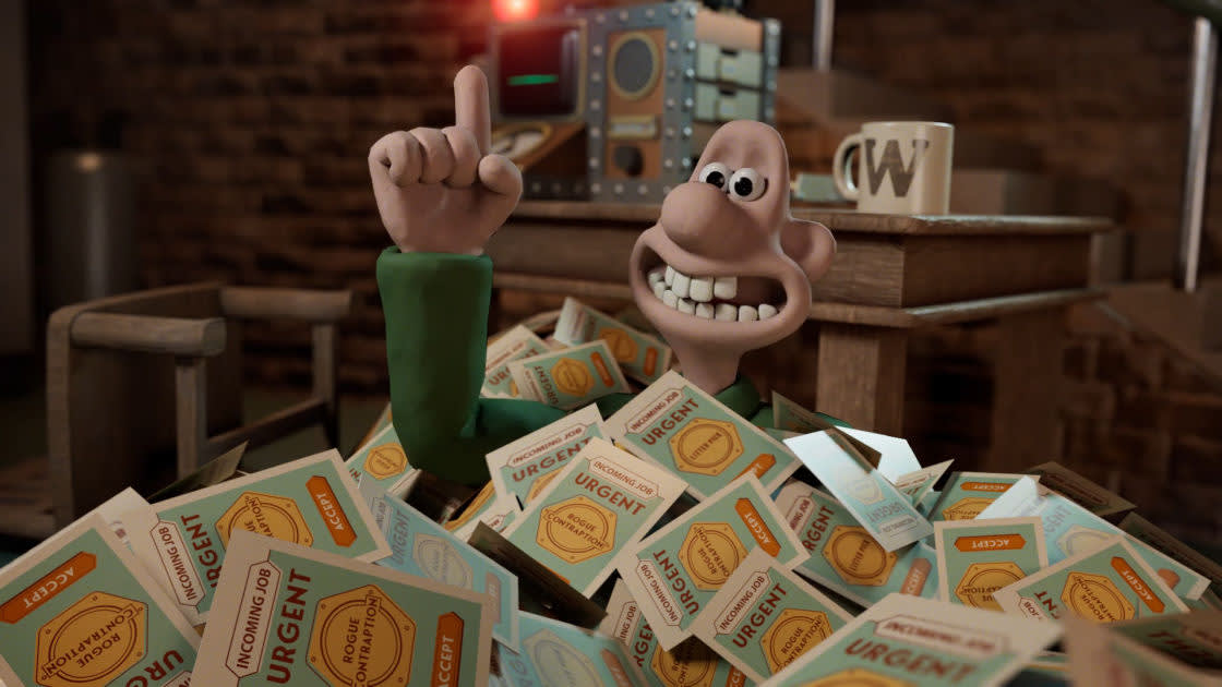 A claymation character with a big smile raises one finger while sitting in a pile of envelopes marked URGENT. Behind him are a mug labeled W, some papers, and old-fashioned equipment on a wooden desk.