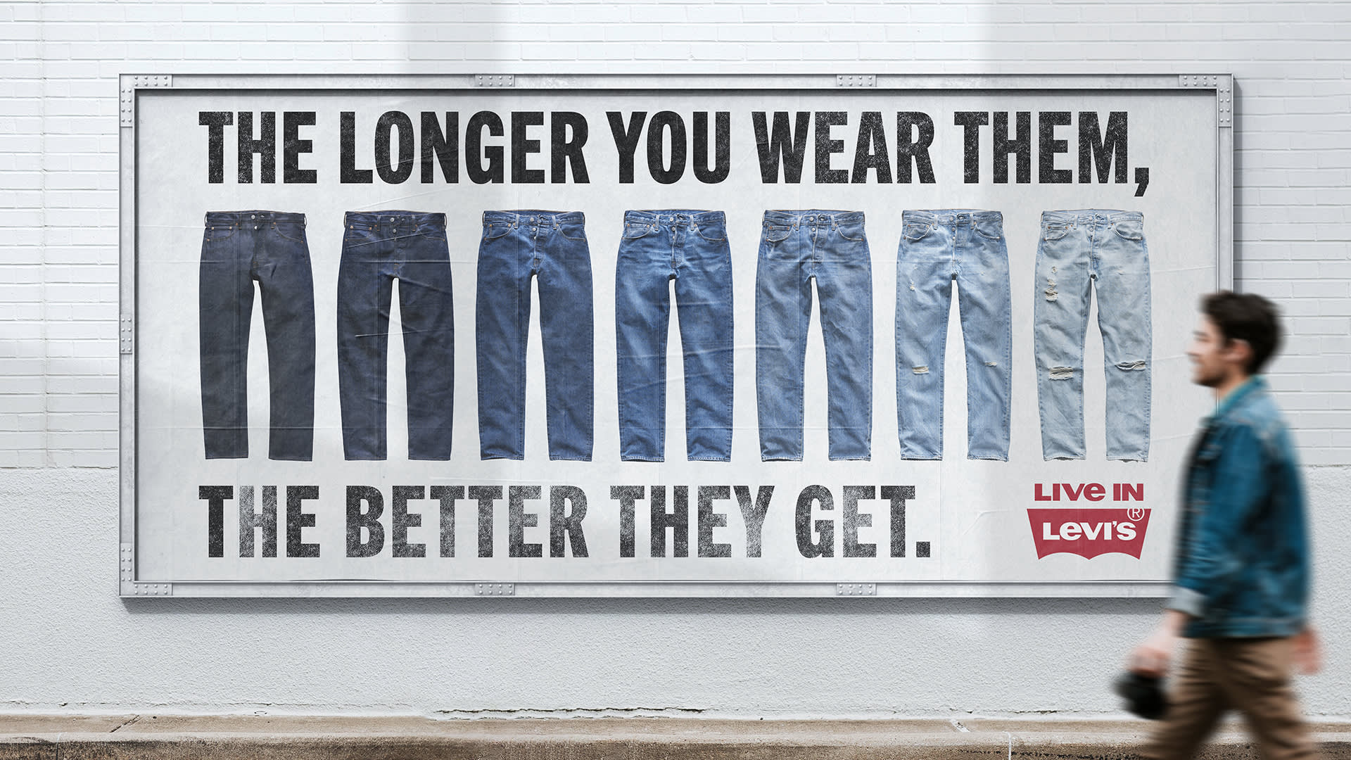 A man walks past a billboard showing six pairs of Levi’s jeans in various stages of wear, with the words The longer you wear them, the better they get. and the Levi’s logo in the corner.