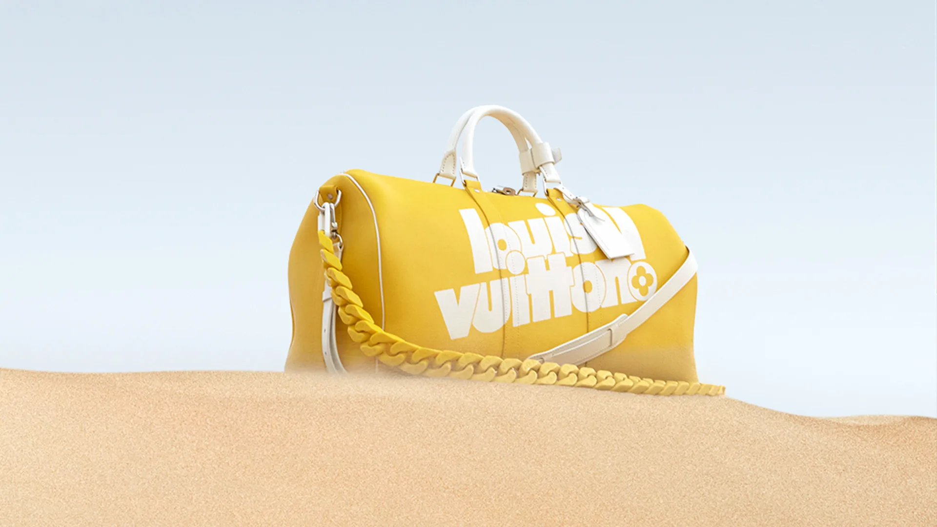 A bright yellow Louis Vuitton duffle bag with bold white logo lettering and a thick yellow chain strap is partially buried in sand against a pale blue sky background.