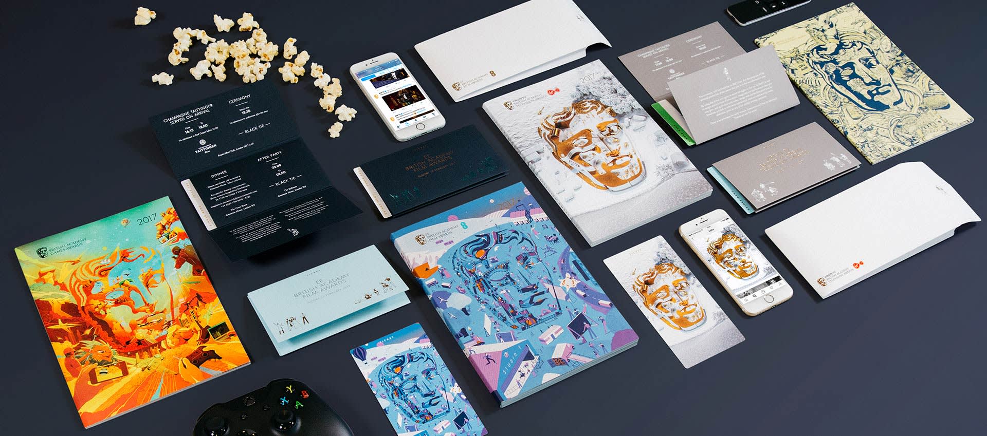 A flat lay of BAFTA-branded materials, including notebooks, brochures, envelopes, smartphones, cards, and a game controller, with scattered popcorn on a dark surface. Each item features stylized BAFTA mask designs.