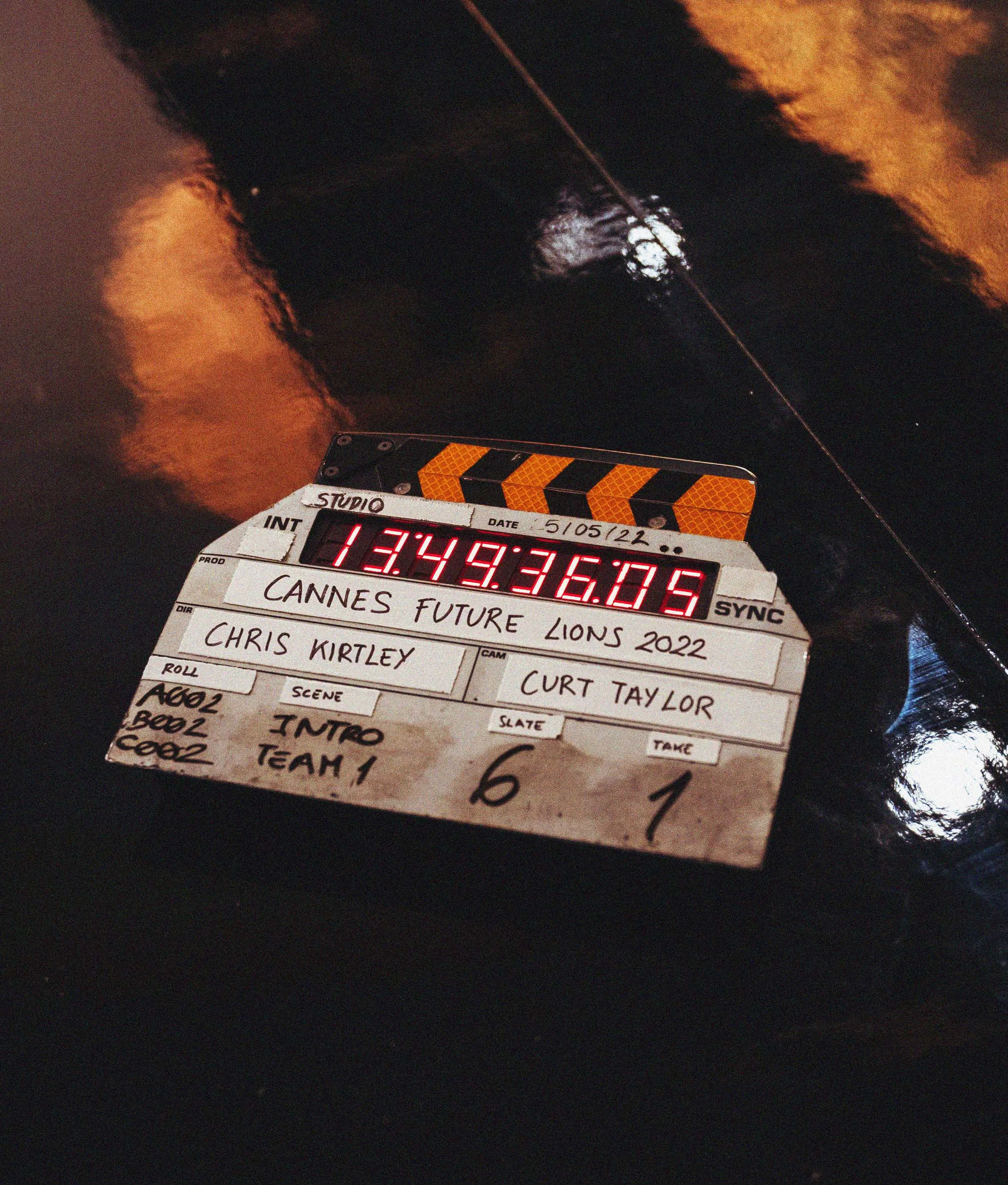 A film clapperboard labeled Cannes Future Lions 2022 rests on a shiny floor. It displays digital time code and handwritten notes about the roll, scene, take, and crew names.