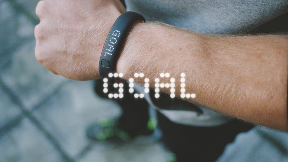A person wearing a fitness tracker displaying GOAL on the screen, indicating they have achieved their activity target. The person is outdoors and dressed in athletic wear.