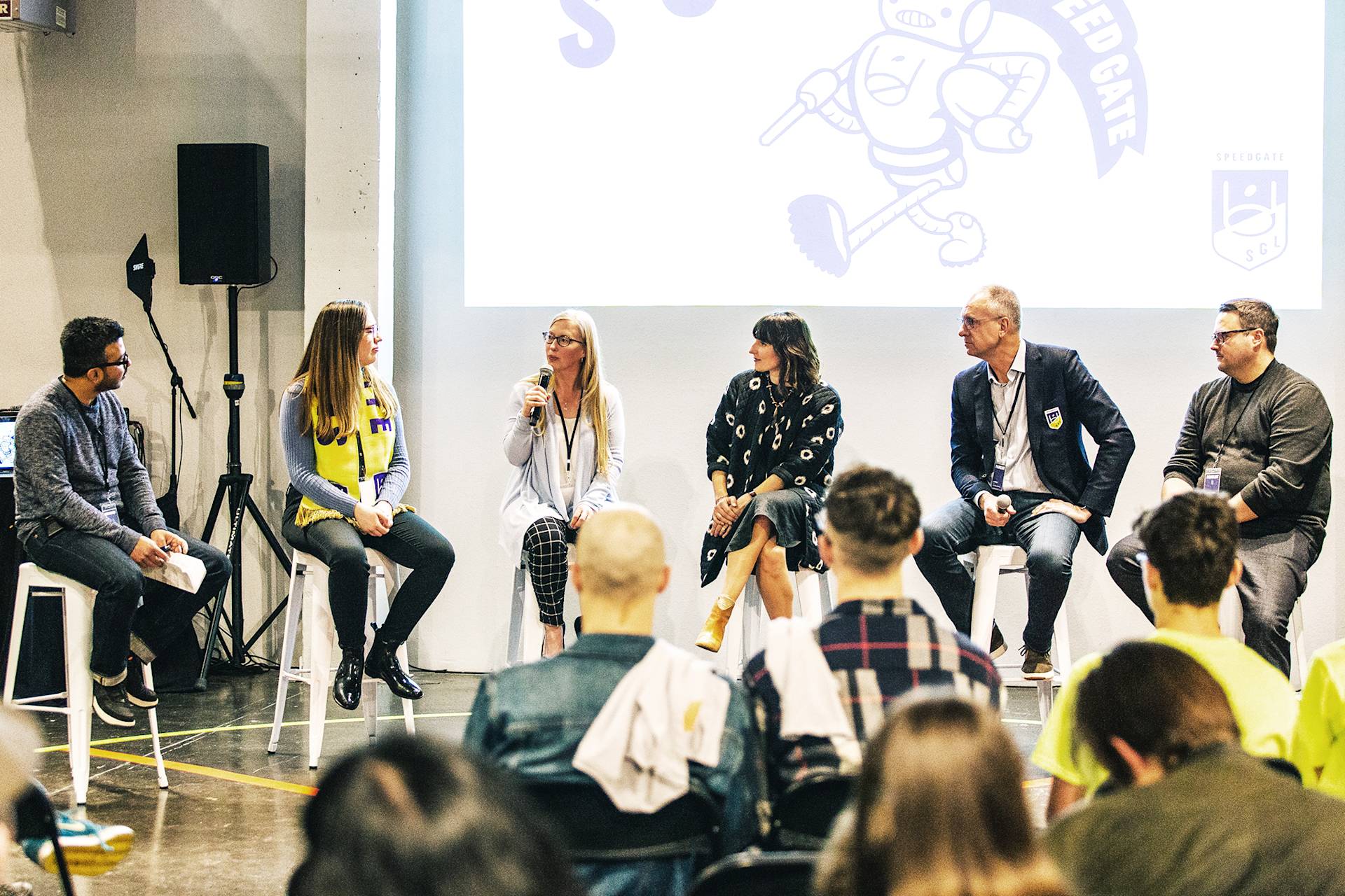 A panel of six people sit in front of an audience.