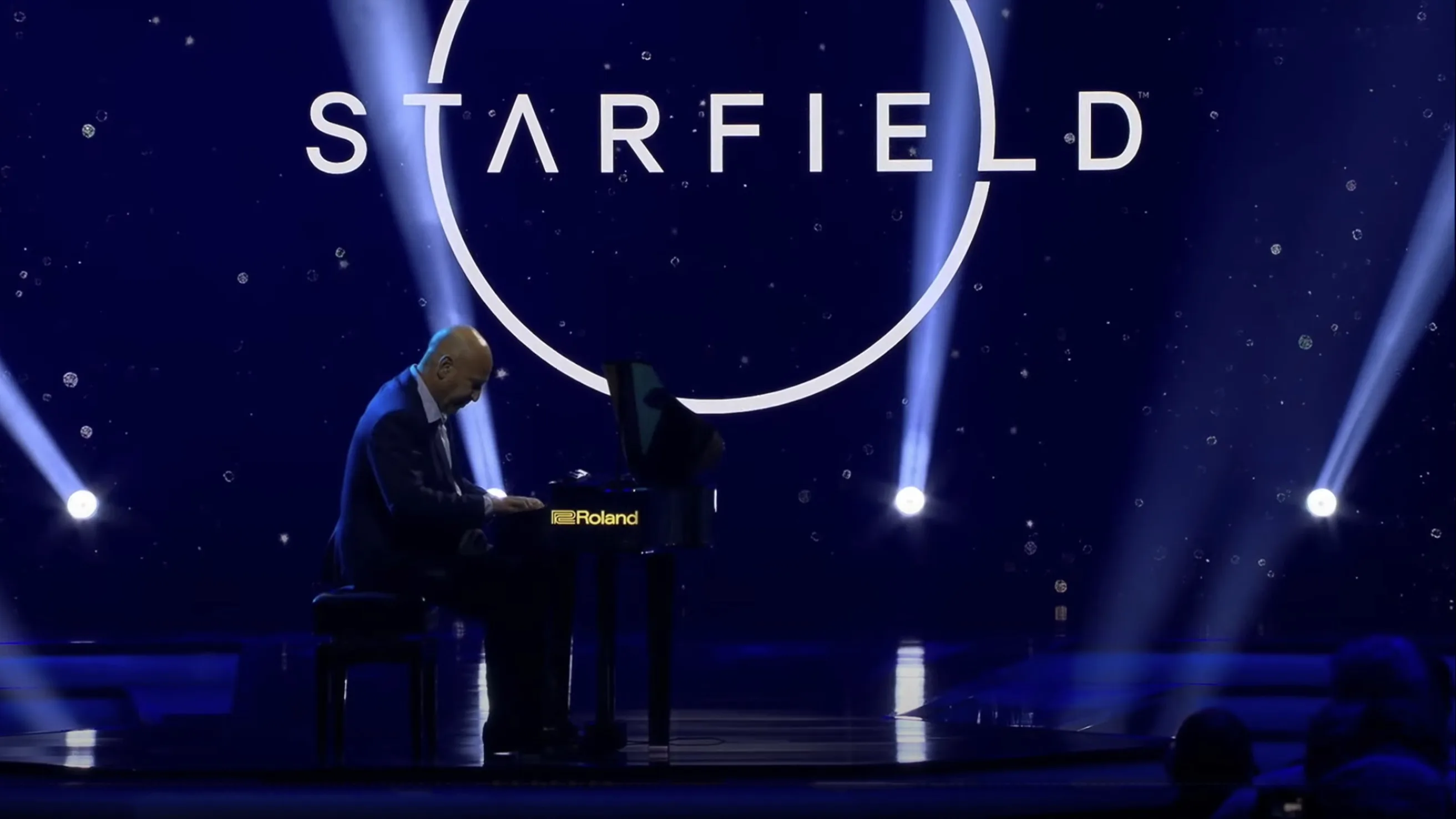 A person plays a Roland grand piano on stage under blue lights, with a large STARFIELD logo and a circular design displayed on a screen in the background.
