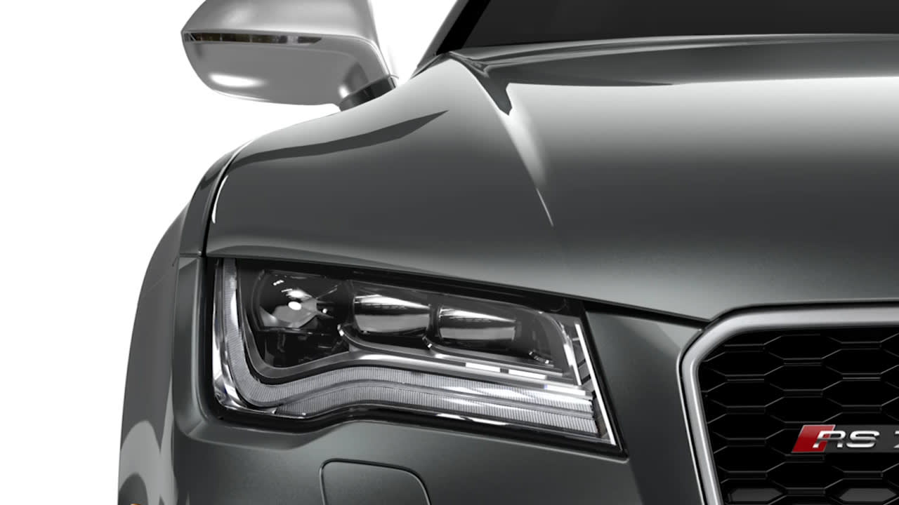 Close-up view of the front left side of a grey Audi RS7, highlighting the headlight, side mirror, and part of the grille with the RS7 badge.