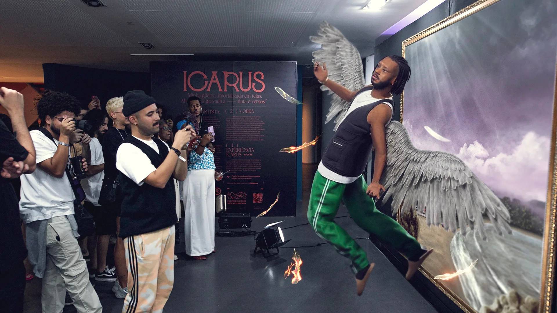 A man wearing fake wings poses as if flying in front of a large Icarus-themed artwork. Several people watch and take photos, capturing the dramatic scene with feathers and flames added for effect.