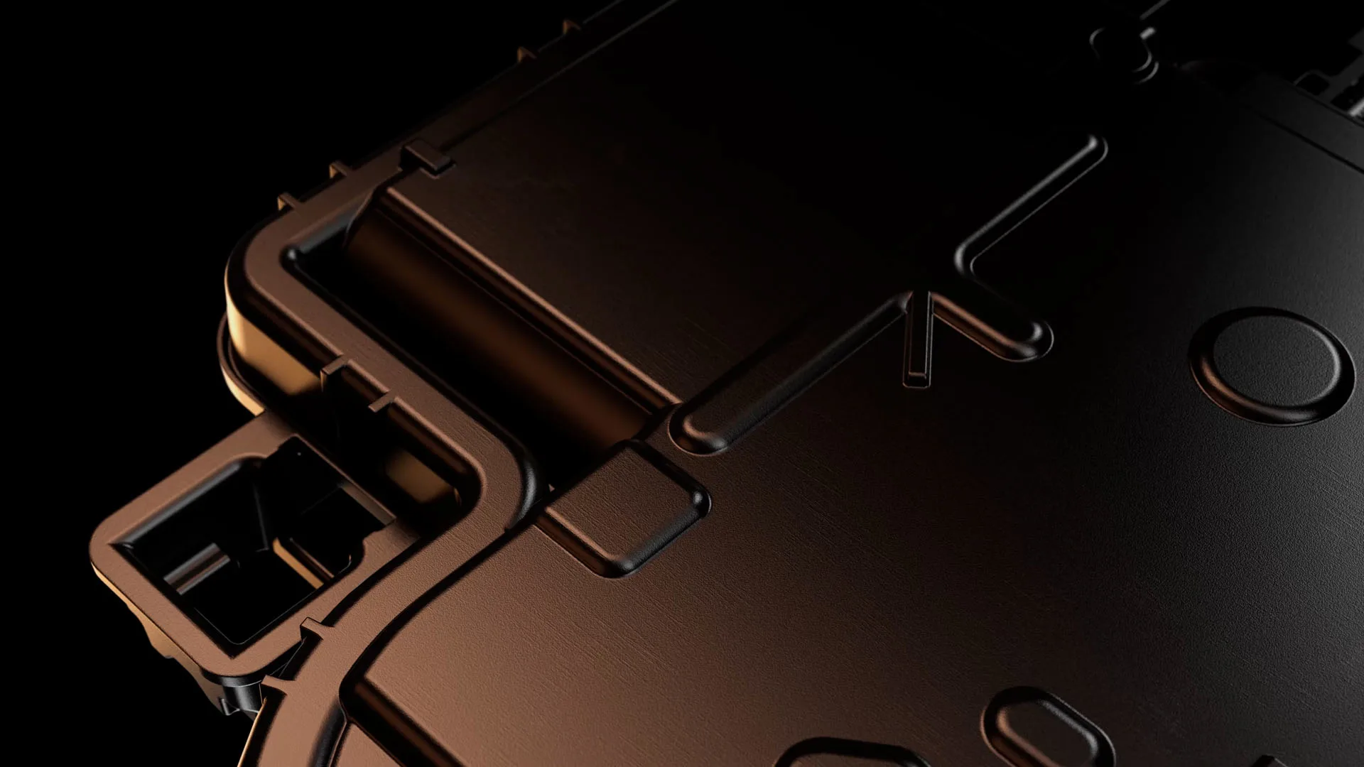 Close-up of a sleek, black metallic surface with geometric patterns, grooves, and raised edges, possibly part of an electronic device or machinery, shown against a dark background.