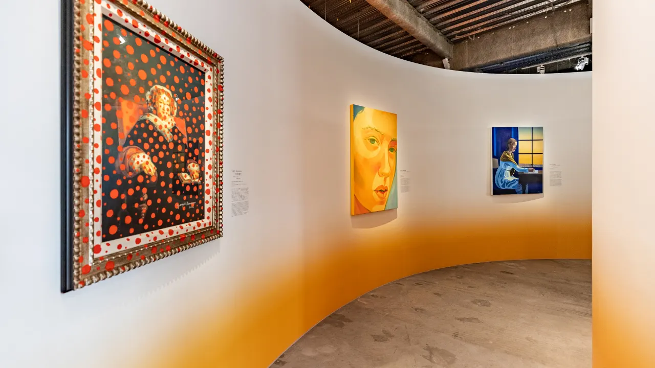 A curved gallery wall displays three colorful paintings: a portrait with red dots, a close-up face with yellow tones, and a blue-hued figure by a window under an industrial ceiling with pipes.