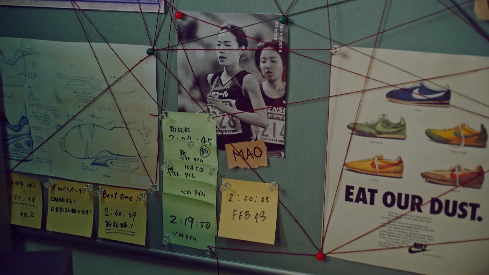 A bulletin board with photos, notes, and running statistics connected by red string. Includes a photo of two female runners, an advertisement for a running shoe, and several handwritten sticky notes with times and diagrams.