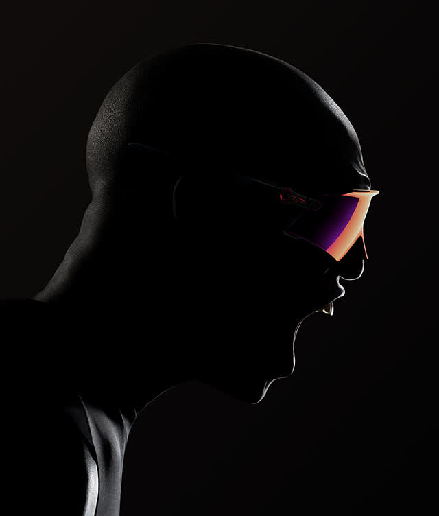 A dramatic side profile of a person in a black bodysuit, mouth open as if shouting, wearing large, reflective, futuristic sunglasses against a dark background.