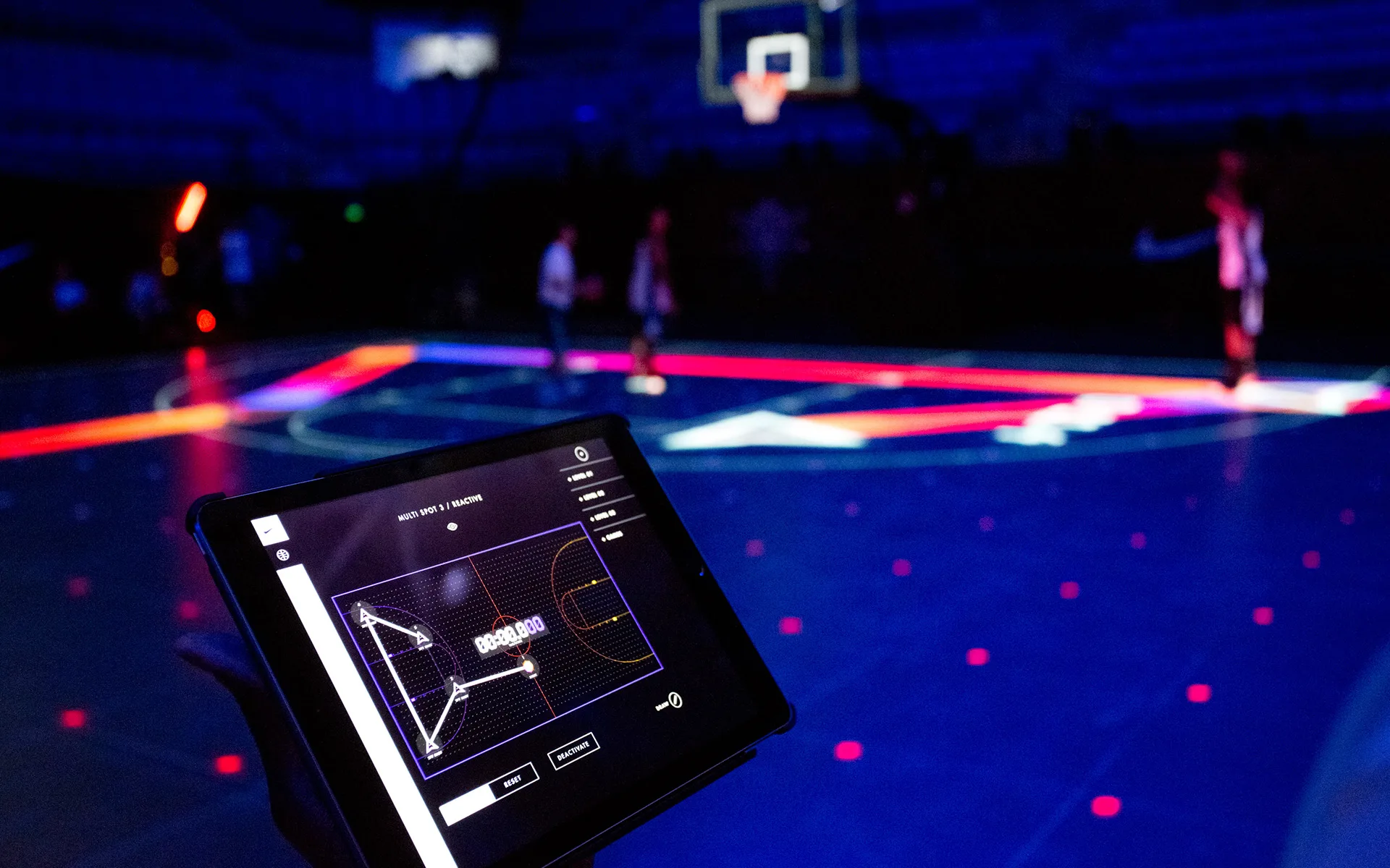 A person holds a tablet displaying basketball analytics, while a high-tech basketball court with glowing digital lines and players in the background is illuminated in blue and red lights.