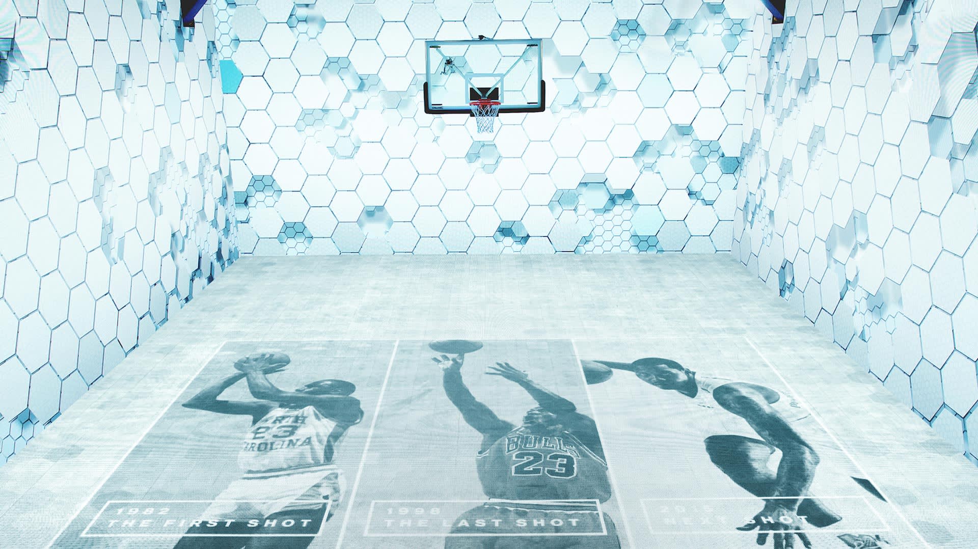 A basketball court with hexagonal patterned walls and floor. Three large images of a player shooting, labeled 1982 The First Shot, 1998 The Last Shot, and 1988 The Shot, are printed on the court floor.