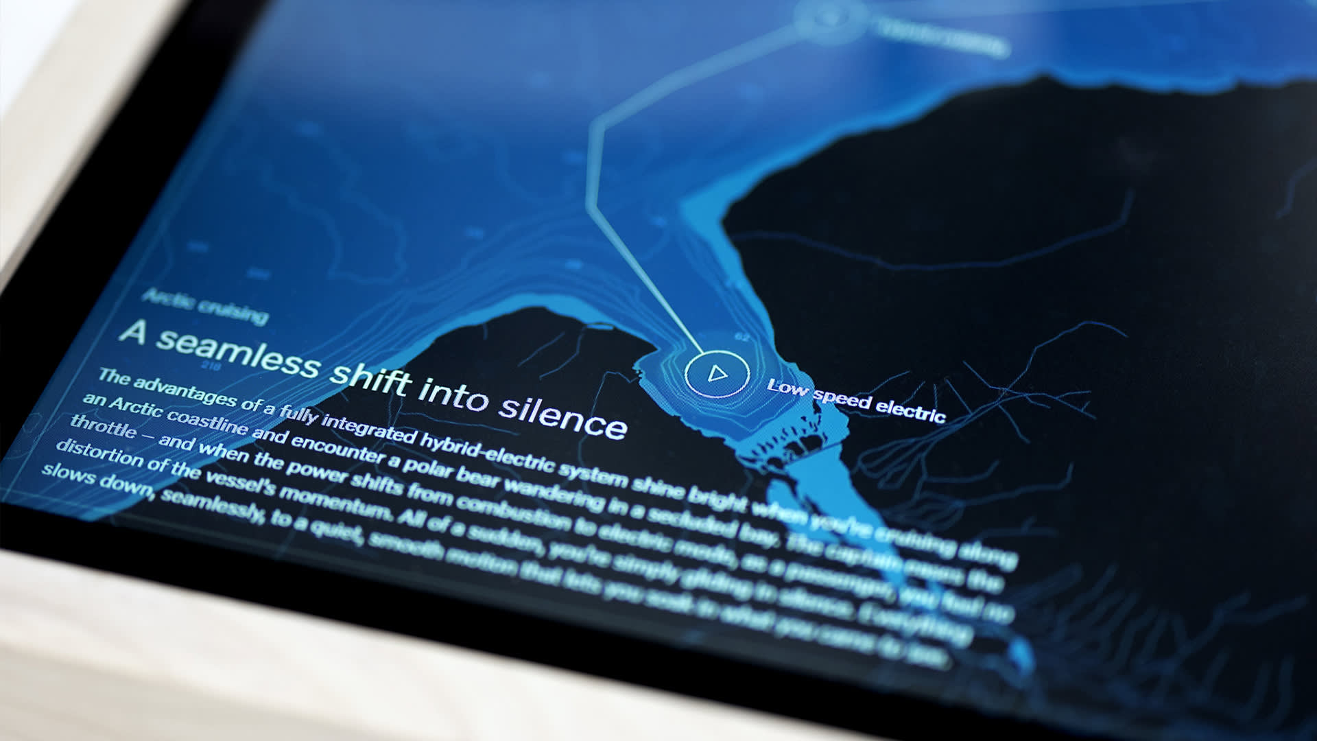 A digital display shows a map with highlighted routes and text titled “A seamless shift into silence,” describing a hybrid-electric system and silent Arctic cruising, alongside a play button icon.