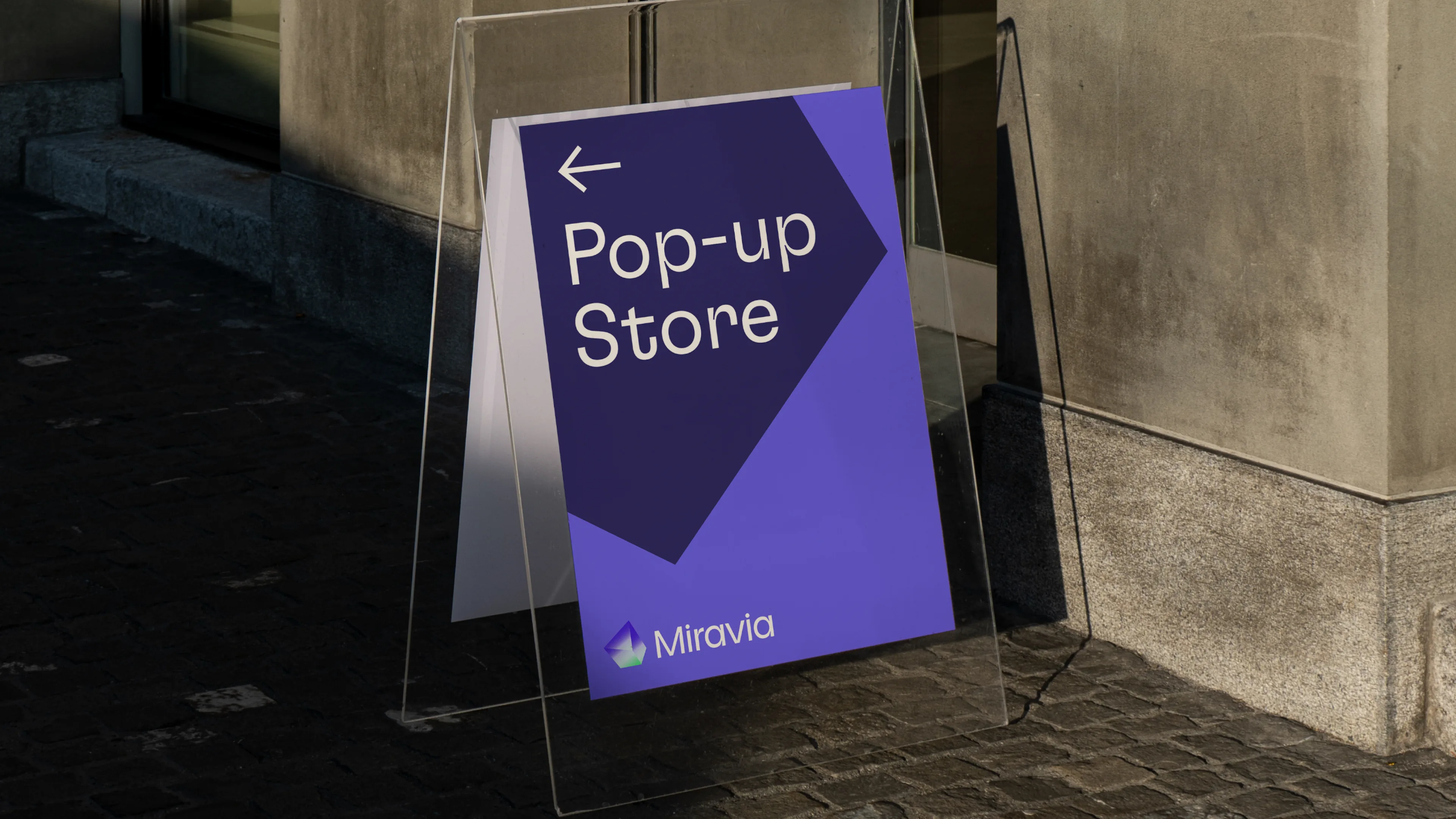 A purple and blue sign reading Pop-up Store with an arrow pointing left and the logo Miravia stands on a sidewalk against a stone building wall.