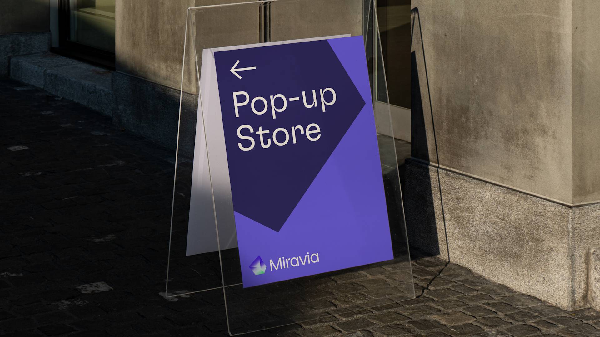 A purple and blue sign reading Pop-up Store with an arrow pointing left and the logo Miravia stands on a sidewalk against a stone building wall.