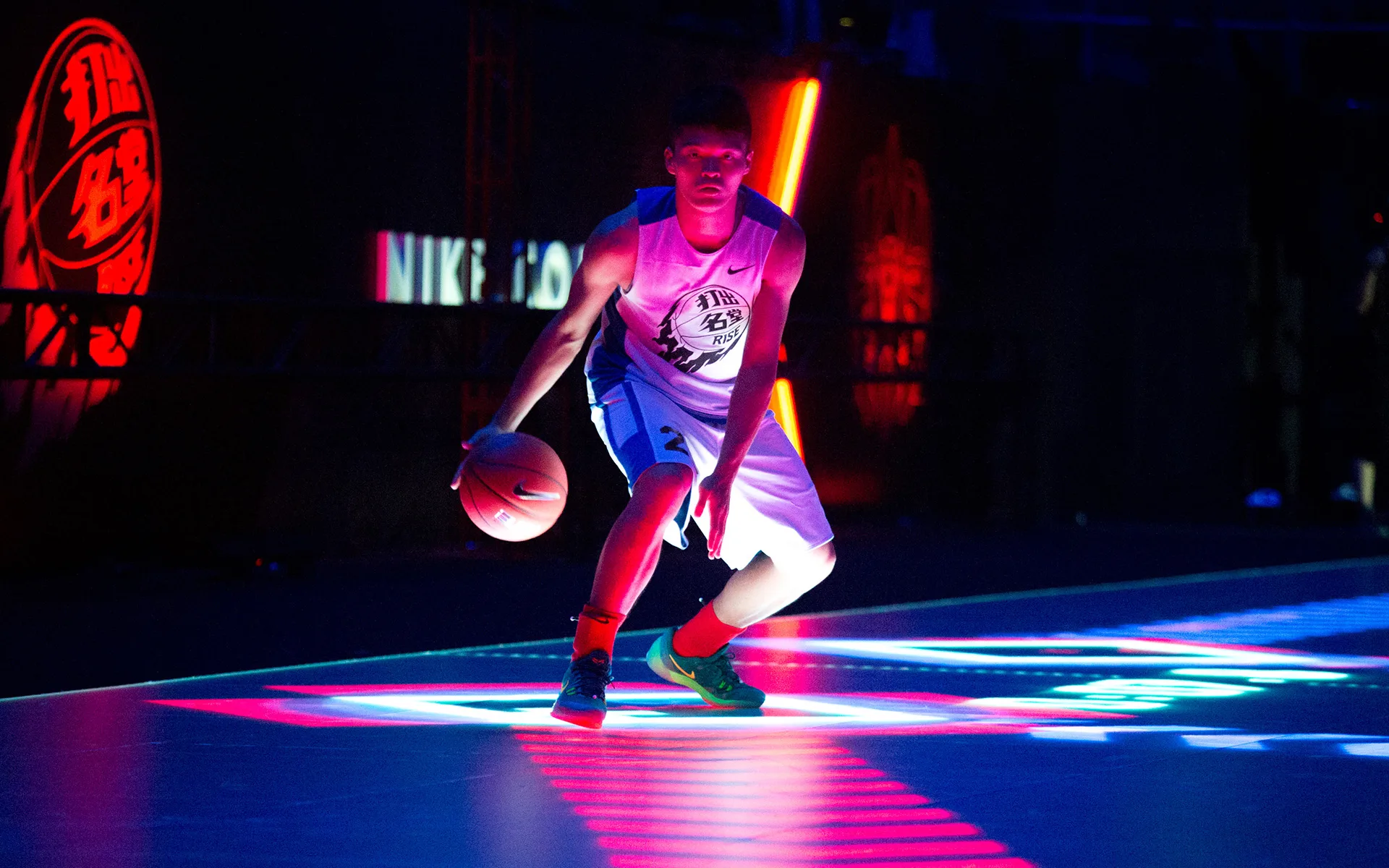 A basketball player dribbles a ball on a dark court with colorful, dramatic lighting and neon reflections, creating a vibrant and intense atmosphere.