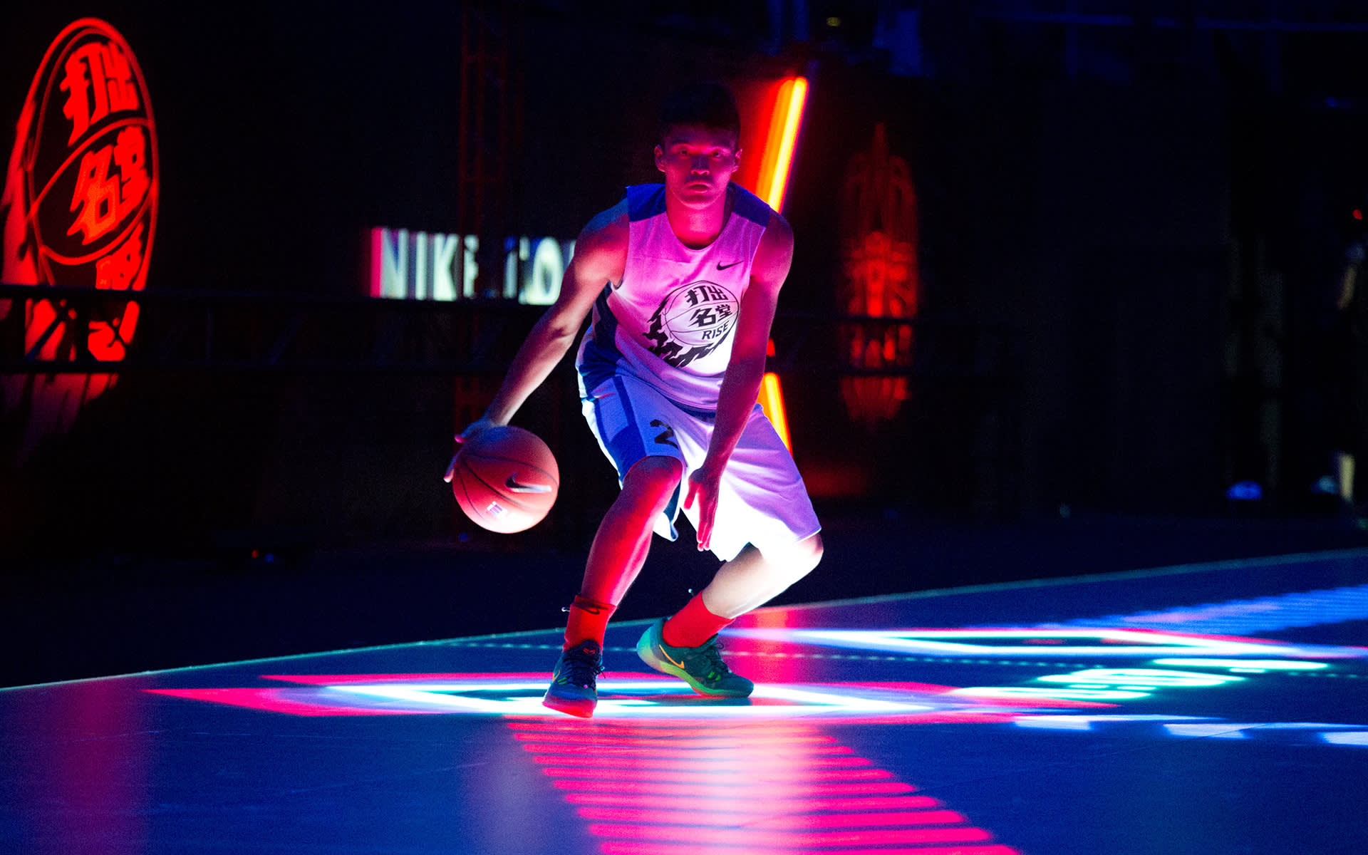 A basketball player dribbles a ball on a dark court with colorful, dramatic lighting and neon reflections, creating a vibrant and intense atmosphere.