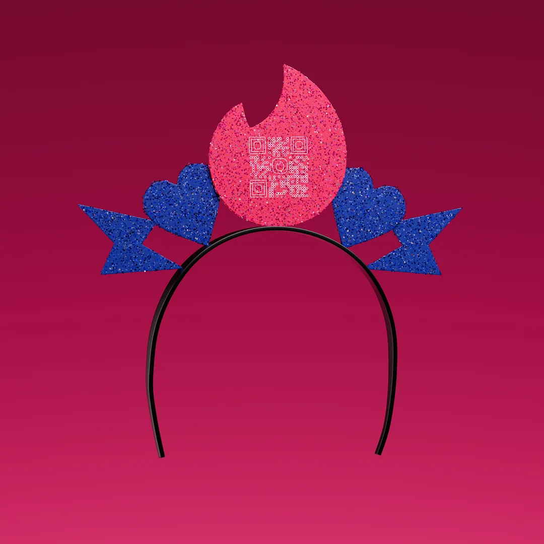 A glittery headband with a large pink flame and two blue hearts with arrows sits against a gradient red background. The flame has a QR code in the center. The headband’s outline suggests it’s meant to be worn.