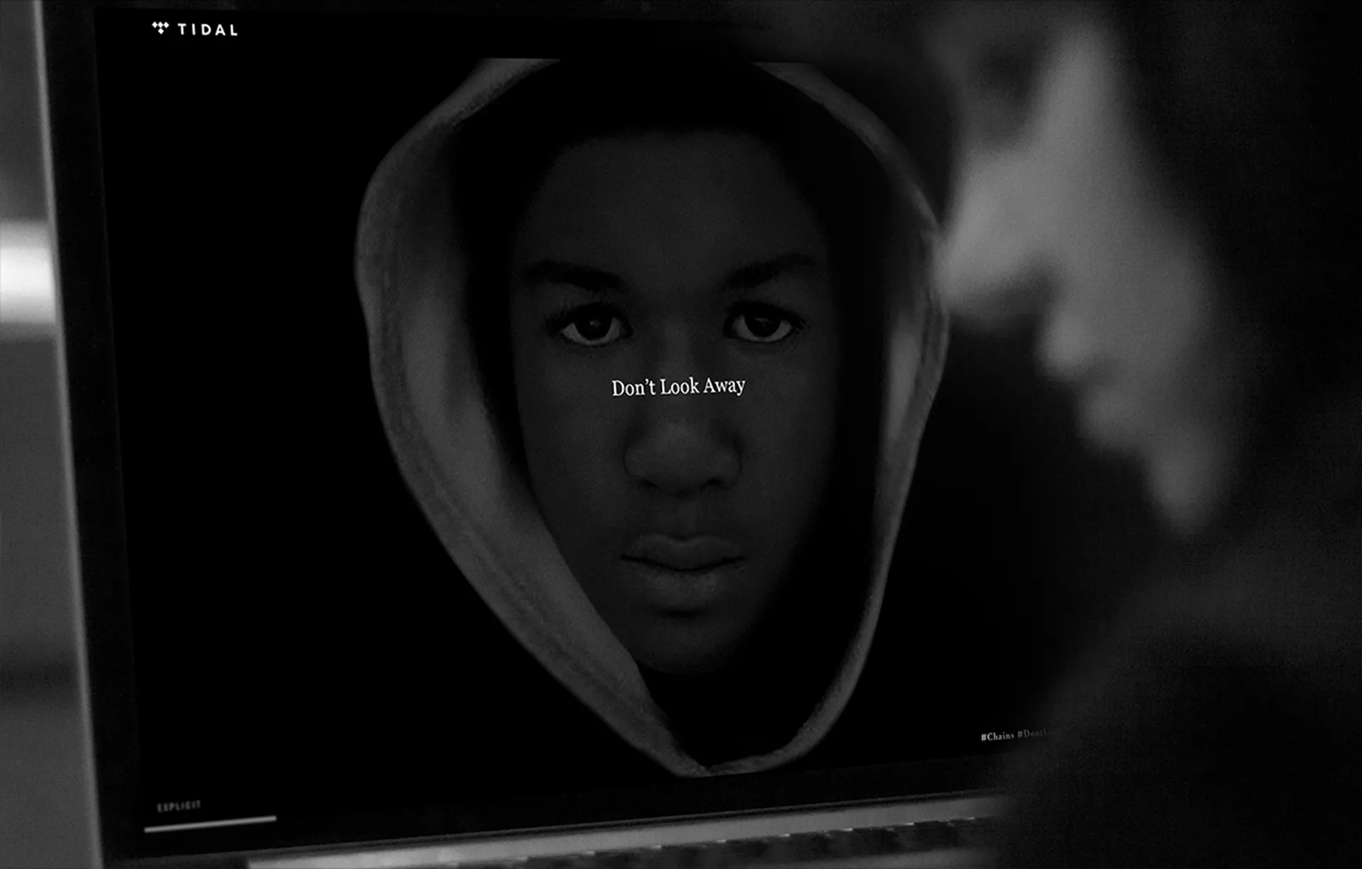 A black-and-white image on a computer screen shows a young person in a hoodie staring ahead. Text overlay reads Dont Look Away. The blurred profile of another person is visible in the foreground.