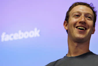 A smiling man stands in front of a blue-purple background with the word facebook partially visible behind him.