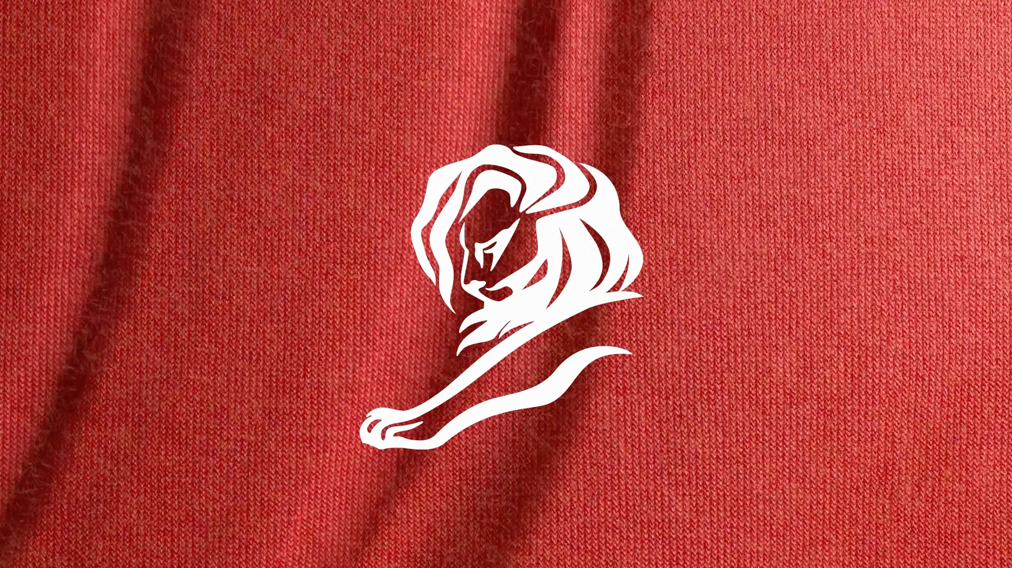 A minimalist white lion head and paw illustration is centered on a textured red fabric background with visible folds.