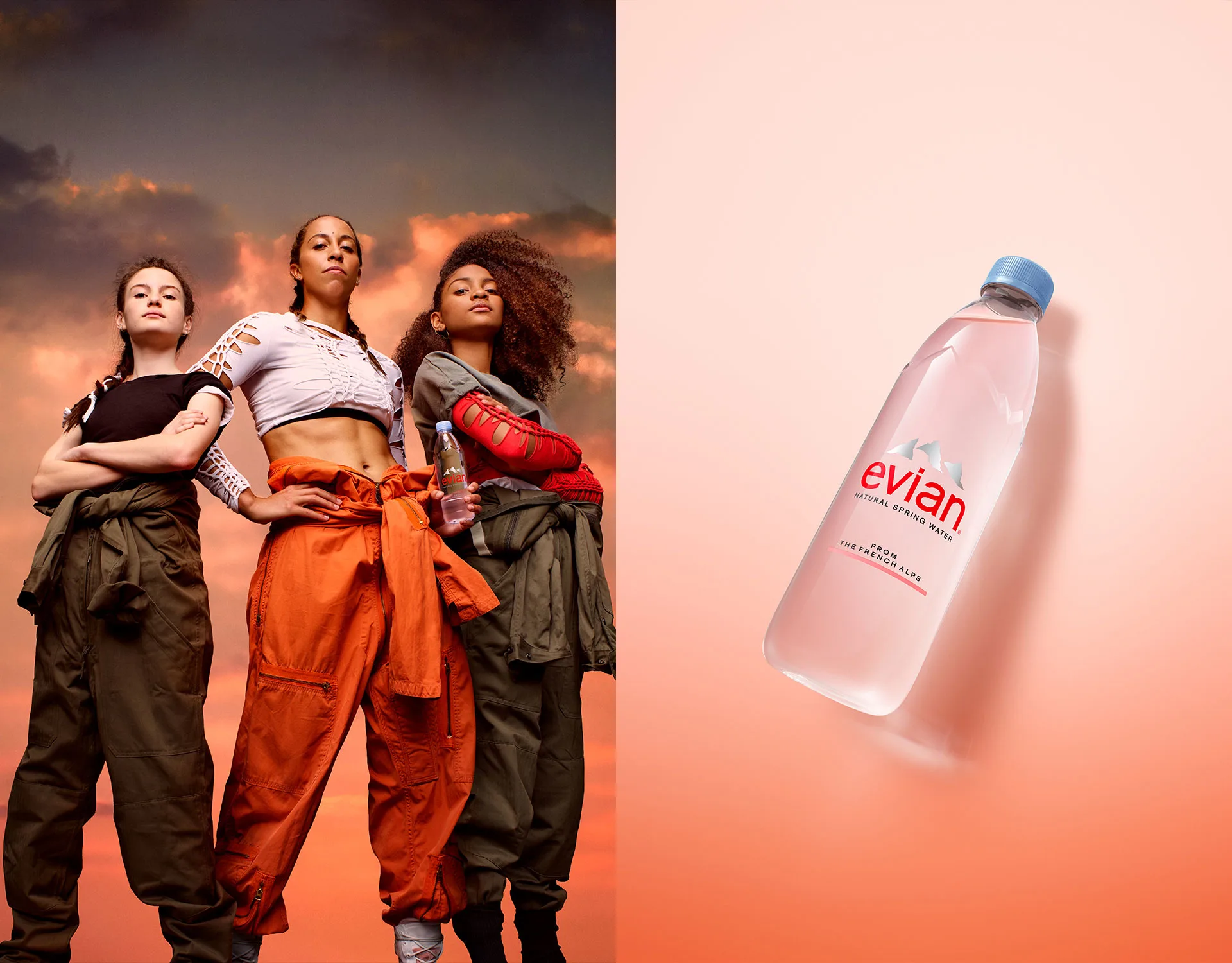 Three confident women in stylish outfits stand with arms crossed against a dramatic sunset sky, next to a clear Evian water bottle on a light pink background.