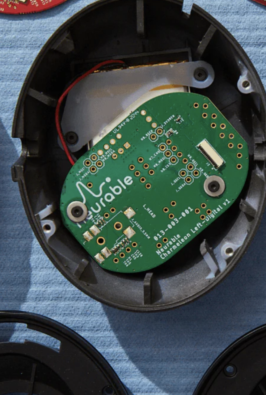 An open black plastic device casing reveals a green circuit board labeled Durable with electronic components and red and black wires, set against a blue fabric background.