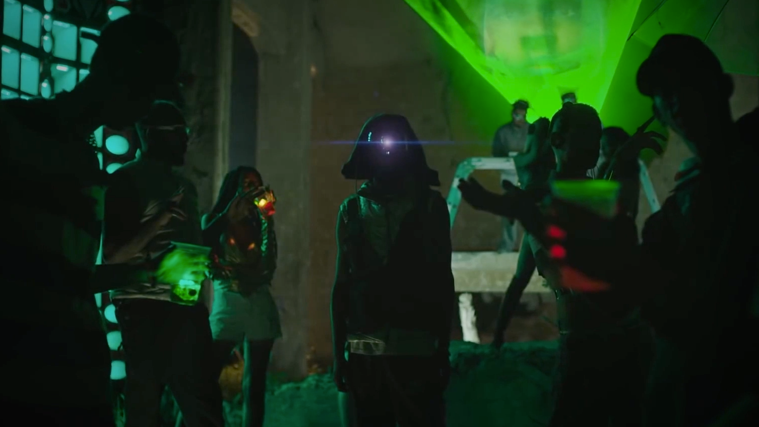 People at a party in a dimly lit room with green neon lights and glowing drinks, some dancing and others standing, creating a futuristic and energetic atmosphere.
