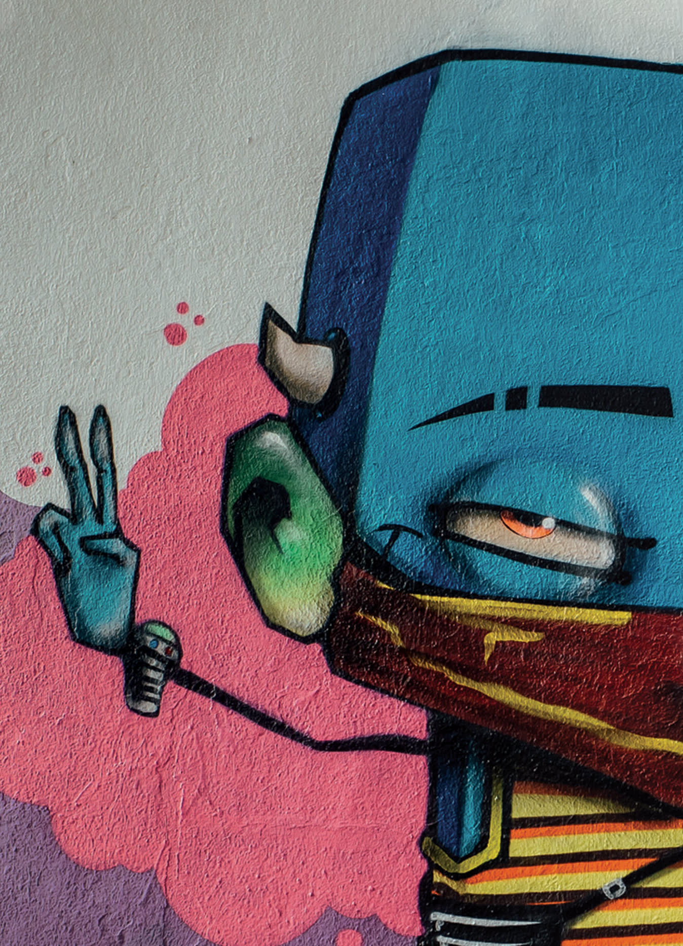 Street art of a cartoonish blue character with a single horn, green ear, and red scarf, holding up two fingers in a peace sign against a textured wall with a pink cloud-like background.