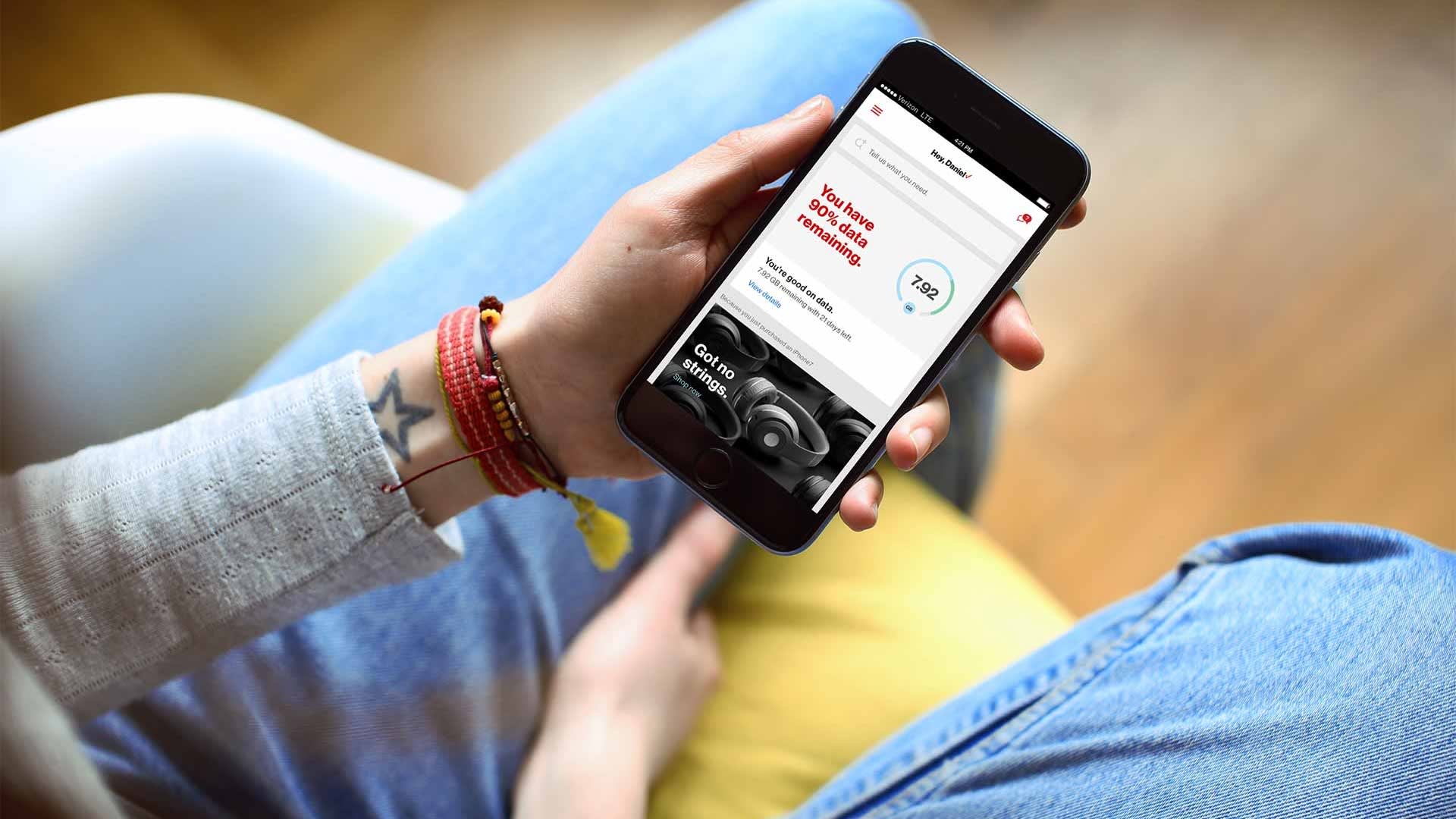 Person holding a smartphone with a health-related app open, displaying a heart rate of 142 BPM, seated on a chair with legs crossed, wearing blue jeans and bracelets.